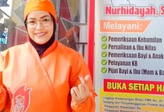 A midwife wearing an orange uniform smiles and poses in front of her private clinic.