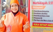 A midwife wearing an orange uniform smiles and poses in front of her private clinic.